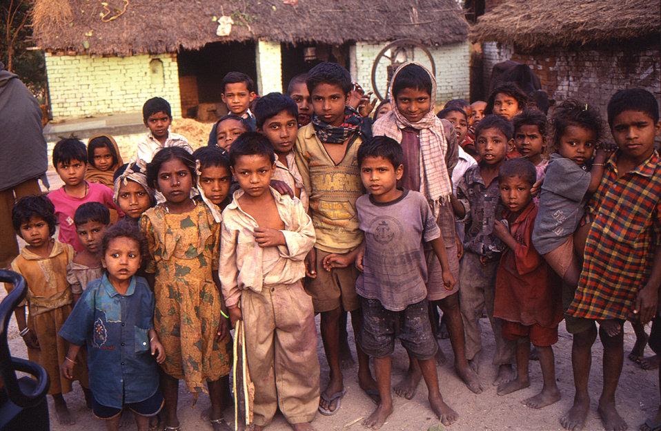 A large group of children gathered outside thatched-roof homes in a rural Indian village
