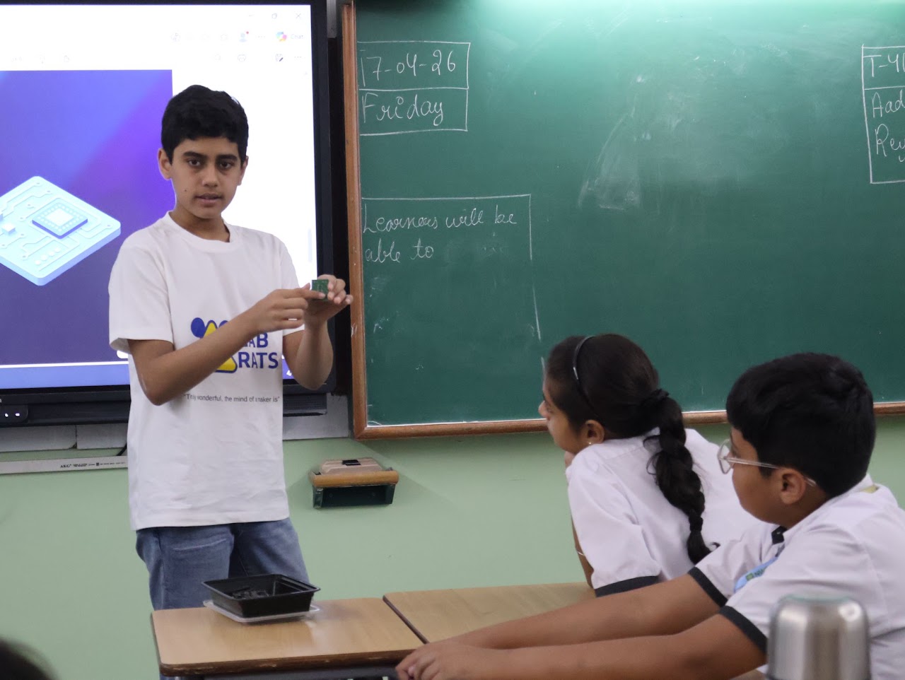 Prashast holding up a small circuit board for two students to see