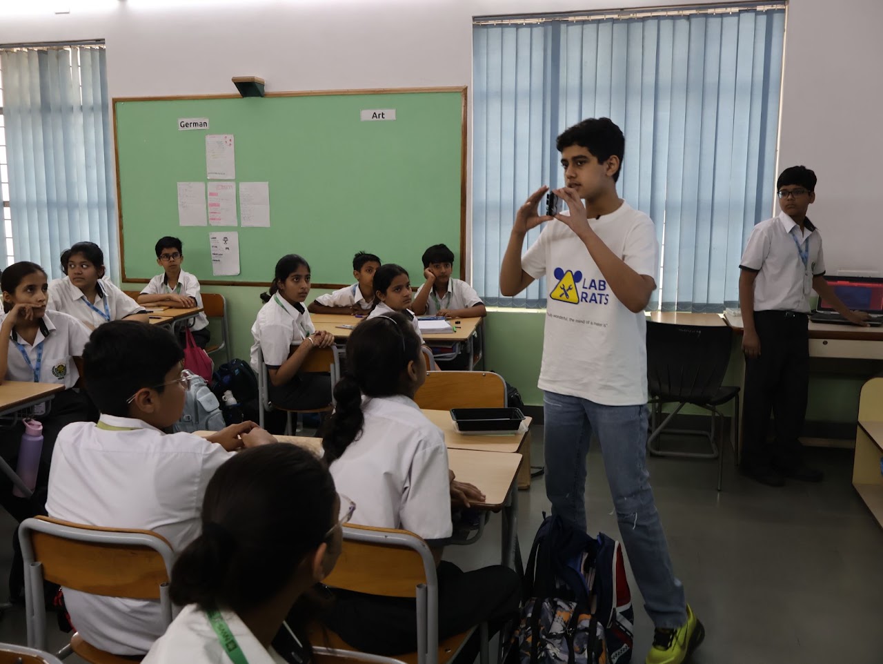Prashast presenting to a seated class beside a green chalkboard